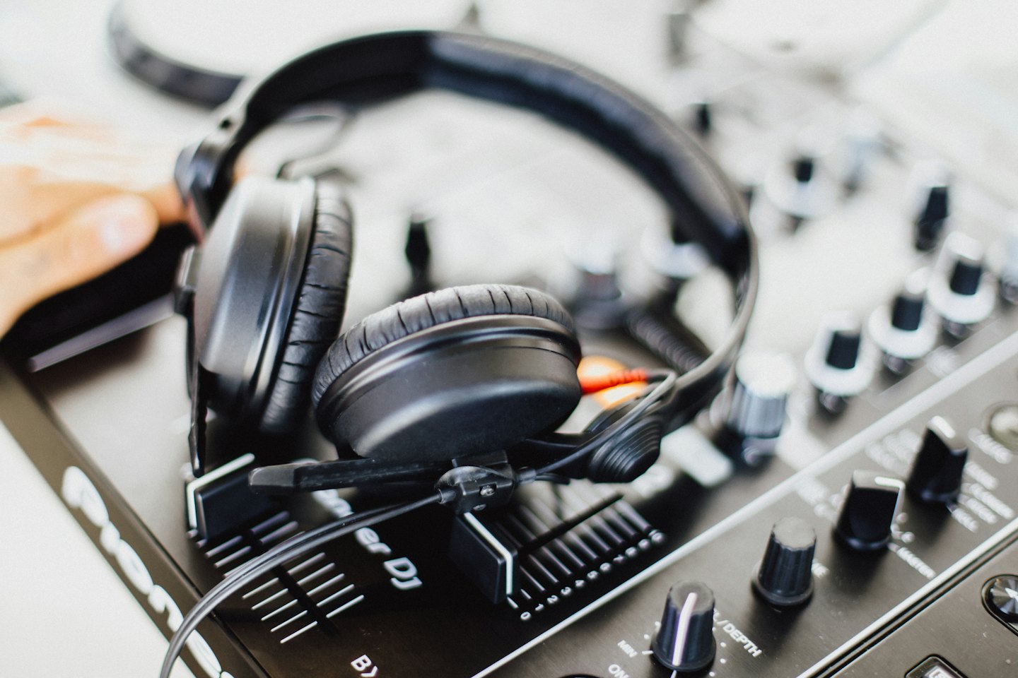 DJ's hand adjusting a mixing console with headphones.
