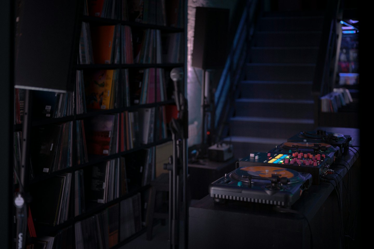 DJ turntables and mixer on a counter with bookshelves of vinyl records.