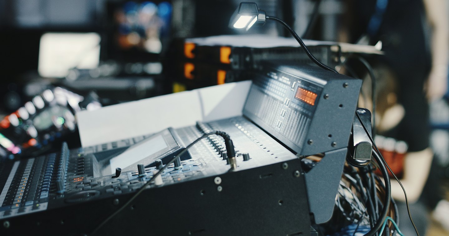 Sound mixing console with faders, knobs, and cables.